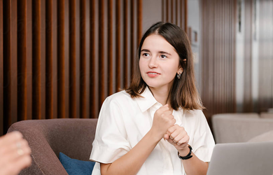 Young woman with laptop sitting on chair speakign to someone in an office environment