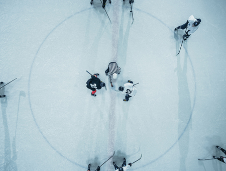 An Ice Hockey Rink With Five Players Actively Engaged In A Game, Skating Across The Ice