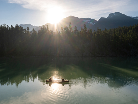 Two People Kayaking In A Lake With A Forest In The Background