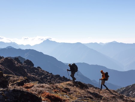 Two Men Climbing A Mountain With Large Mountains In The Background