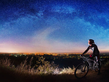 Cyclist Driving Through A Field At Night With Sky Full Of Stars In The Background