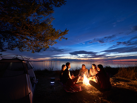 A Group Of Friends Camping By The Lake Next To A Camp Fire