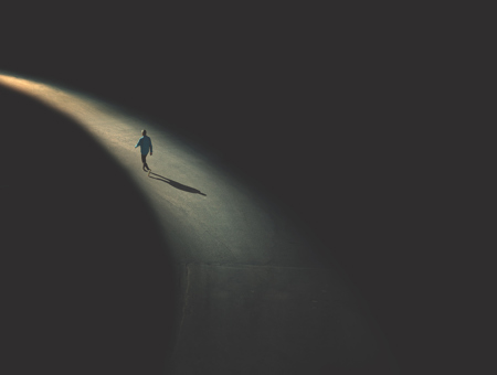  A Man Walking In The Snipped Of Light In The Black Background